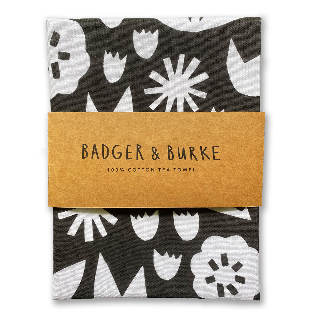 a black and white tea towel featuring an all over floral design inspired by mid century and scandinavian design