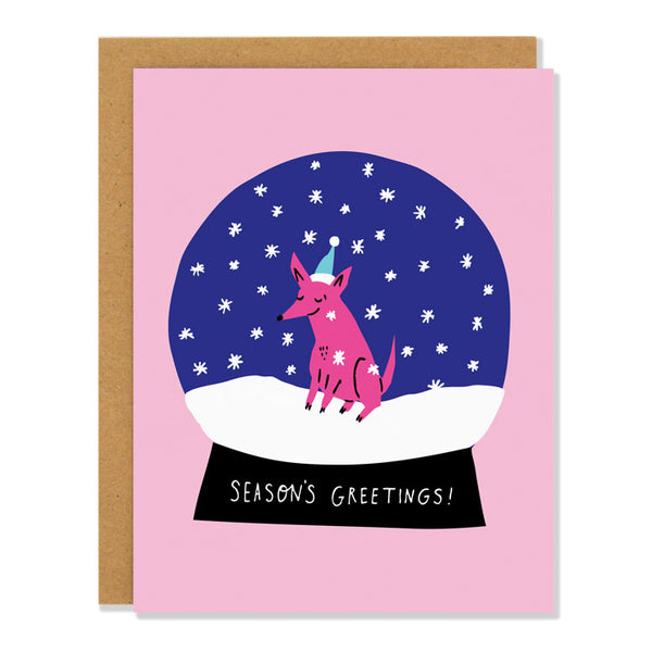 a holiday greeting card featuring a snow globe with a small pink dog sitting in the snow with a smile and a light blue santa hat. The text on the base of the globe reads "Season's Greetings"