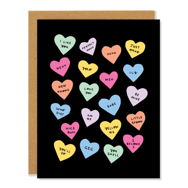 A black greeting card with colorful heart-shaped candies with phrases like "I like you," "perfect match," "XOXO," "Just okay," "YOLO," "Meh," "ILY," "New phone," "Love you," "Be mine," "Who dis?," "Babe," "DM me," "Nice bum," "Yellow #6," "Little spoon," "You'll do," "G2G," "You smell," and "2 become 1."