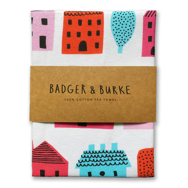 tea towel featuring cutesy illustrated houses and trees in multi colours against a white background