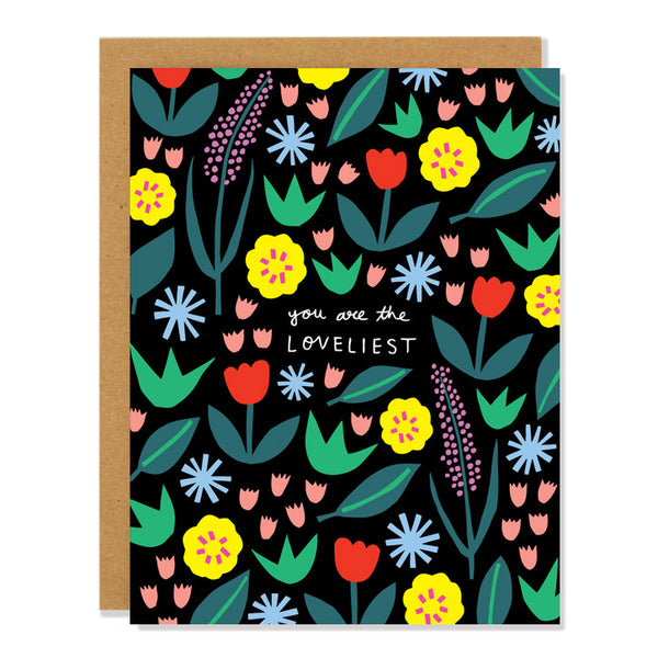 a love and friendship greeting card featuring an all over pattern of multi colored floral designs on a black background. The handwritten text in the middle reads: "You are the Loveliest"