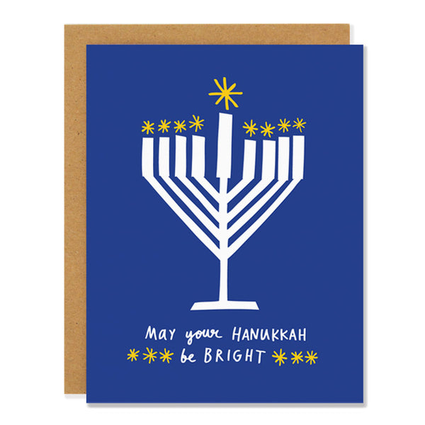 a hanukkah greeting card featuring a 1950s inspired cut out illustration of a menorah on a blue background, lit with yellow stars. Text reads: "may your hanukkah be bright"