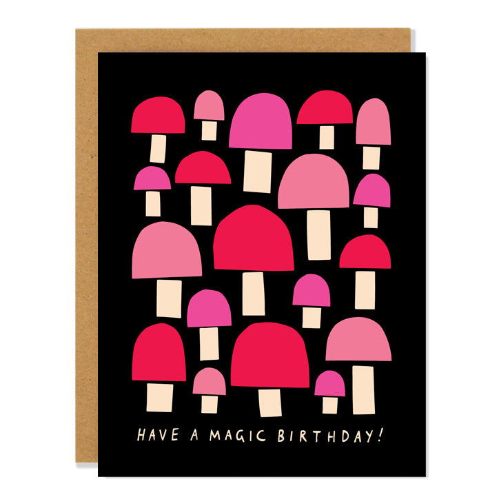 a birthday greeting card with illustrated paper cut out mushrooms in shades of pink and red on a black background, with text that reads: "have a magic birthday!"