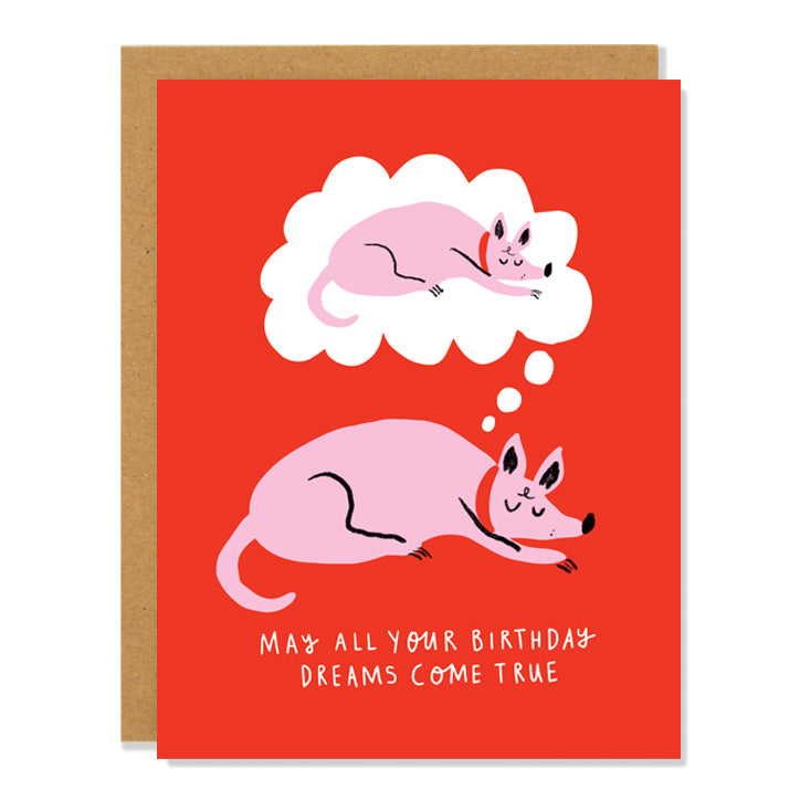 A red birthday card with a cartoon illustration of a pink dog sleeping and dreaming of itself sleeping, and the text "May all your birthday dreams come true" written in white at the bottom.