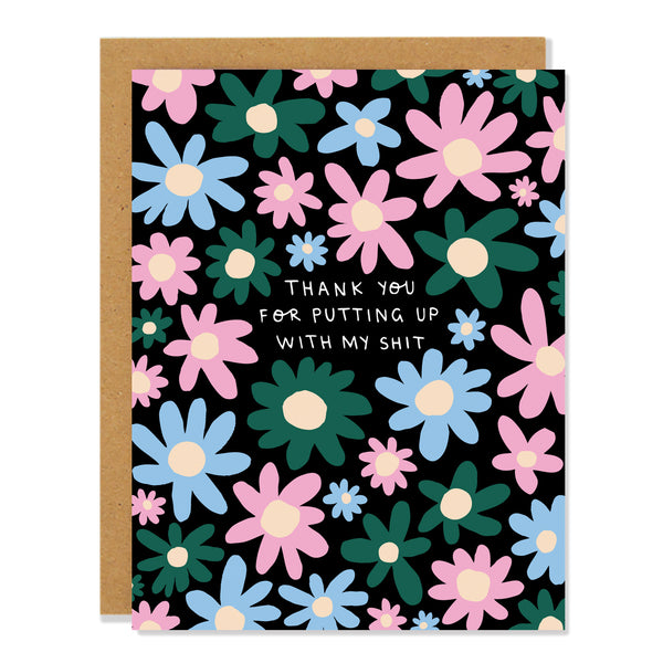 a greeting card with an all over flower pattern featuring multi colored daisies in dark green, baby blue and baby pink on a black background. The text in the middle reads: "thank you for putting up with my shit"