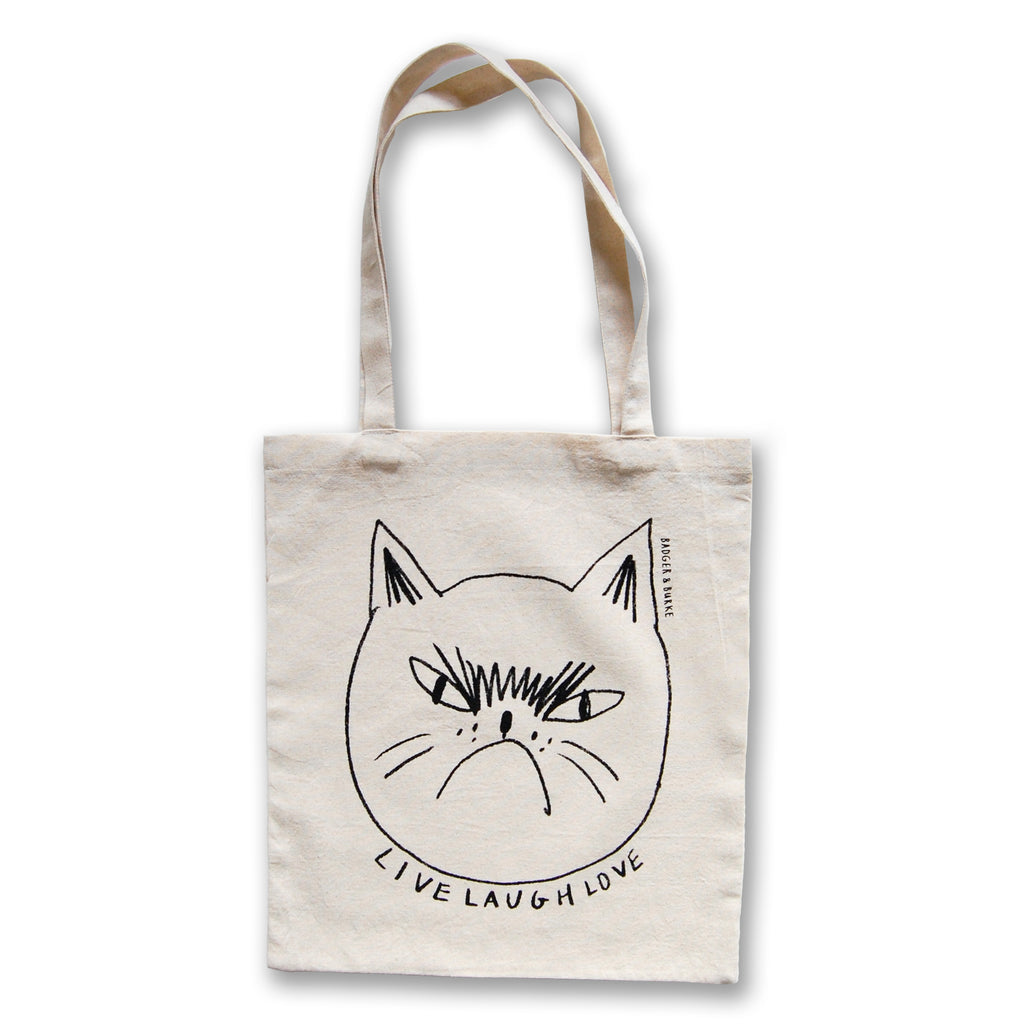 a tote bag with a black line drawing of an angry, grumpy cat with the text "live laugh love" underneath