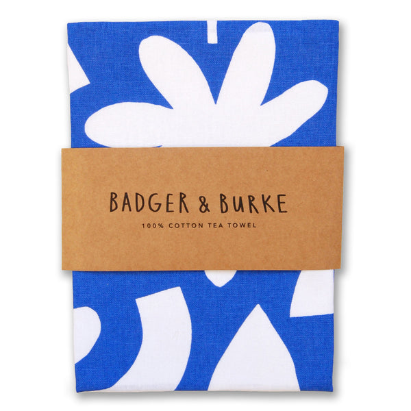 White paper cut-out shapes of leaves, flowers, and abstract designs on a vibrant blue background of a tea towel 