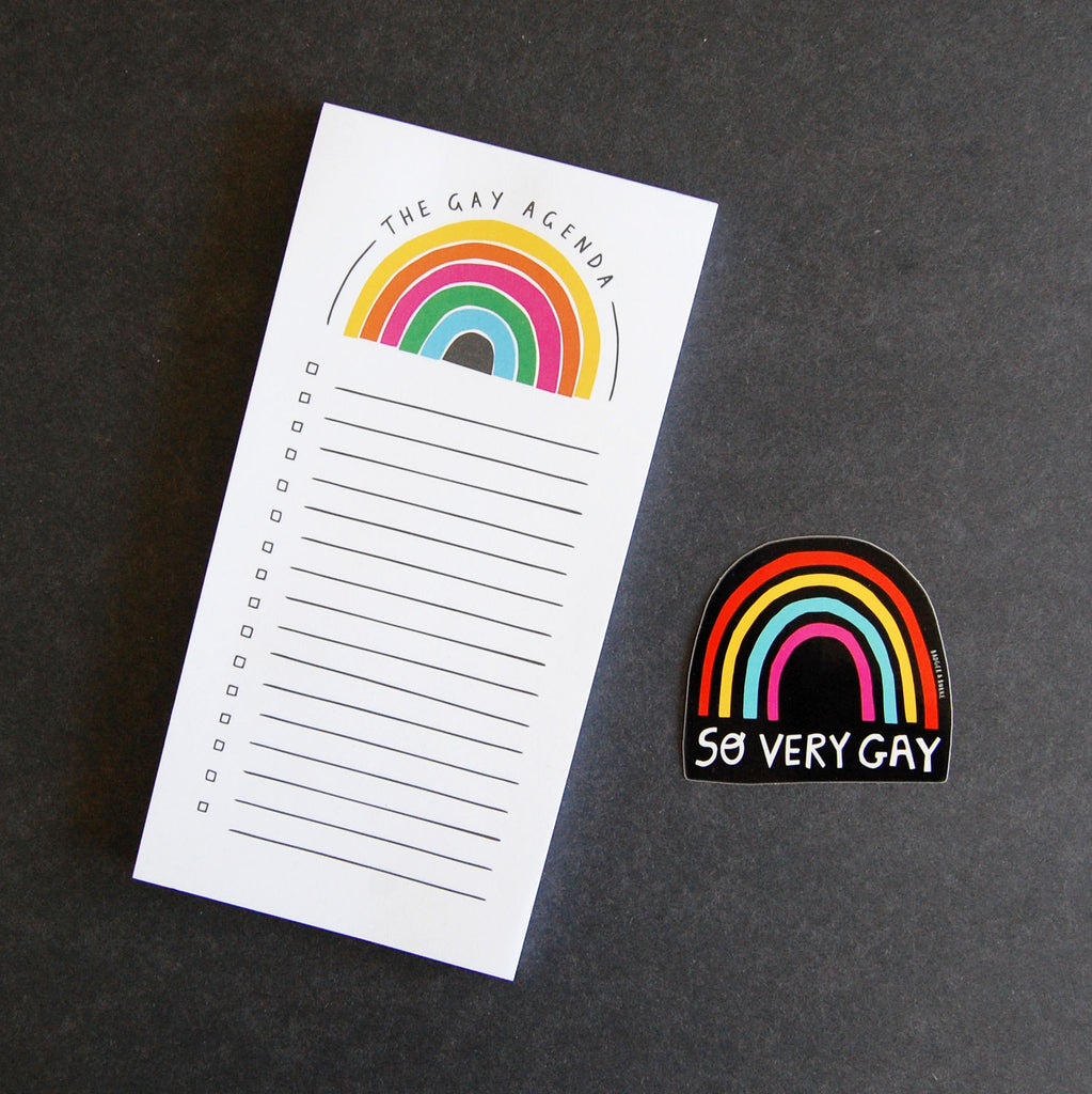 a photo of two stationery products on a black background, first the gay agenda notebook, second a rainbow sticker with text reading "SO VERY GAY"