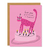 a birthday card featuring an illustration of a pink cat wearing a party hat standing on a light pink birthday cake, having knocked out a number of birthday candles. text reads: hope your birthday is purrfect"