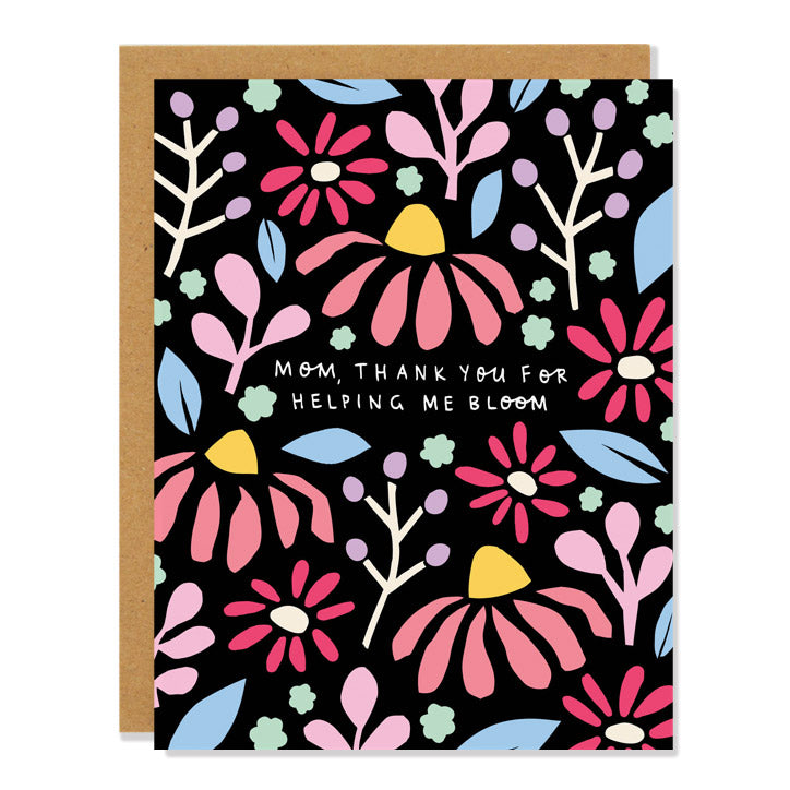 A mother's day greeting card featuring a floral cut out design with coneflowers and blossoms and daisies in pastel colors on a black background. The text reads: Mom, thank you for helping me bloom