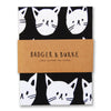 a tea towel featuring an illustration of a multitude of white cat faces on a black background
