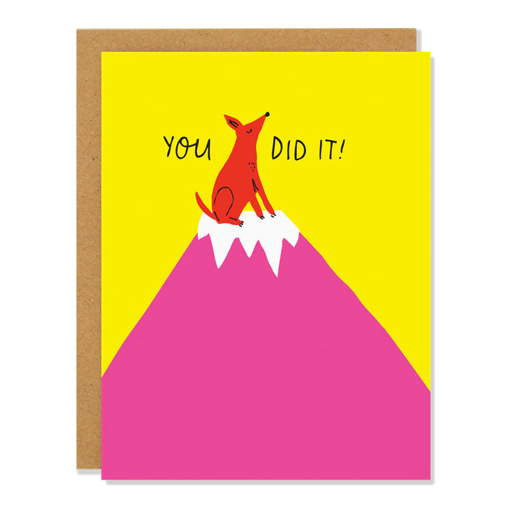 A congratulatory greeting card featuring an illustration of a small red dog on top of a pink snowcapped mountain, against a yellow sky. The text reads: You Did It! 