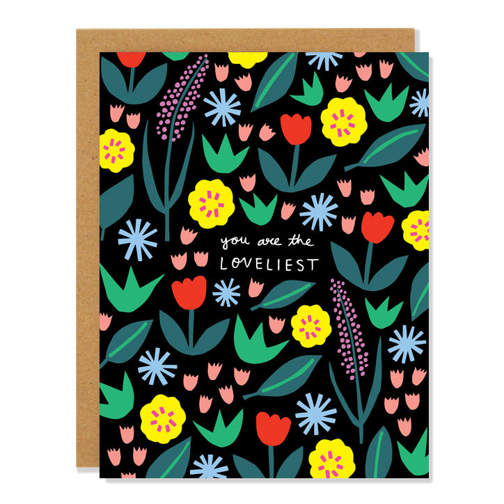 a love and friendship greeting card featuring an all over pattern of multi colored floral designs on a black background. The handwritten text in the middle reads: "You are the Loveliest"  